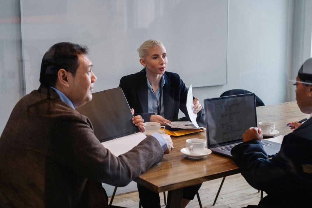 Four people around a wooden table with laptops and coffee cups, one holding up a document.