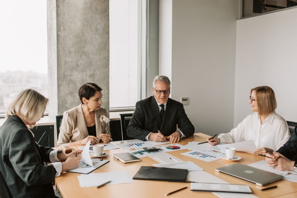 Five people at a long meeting table covered with printed charts and papers.