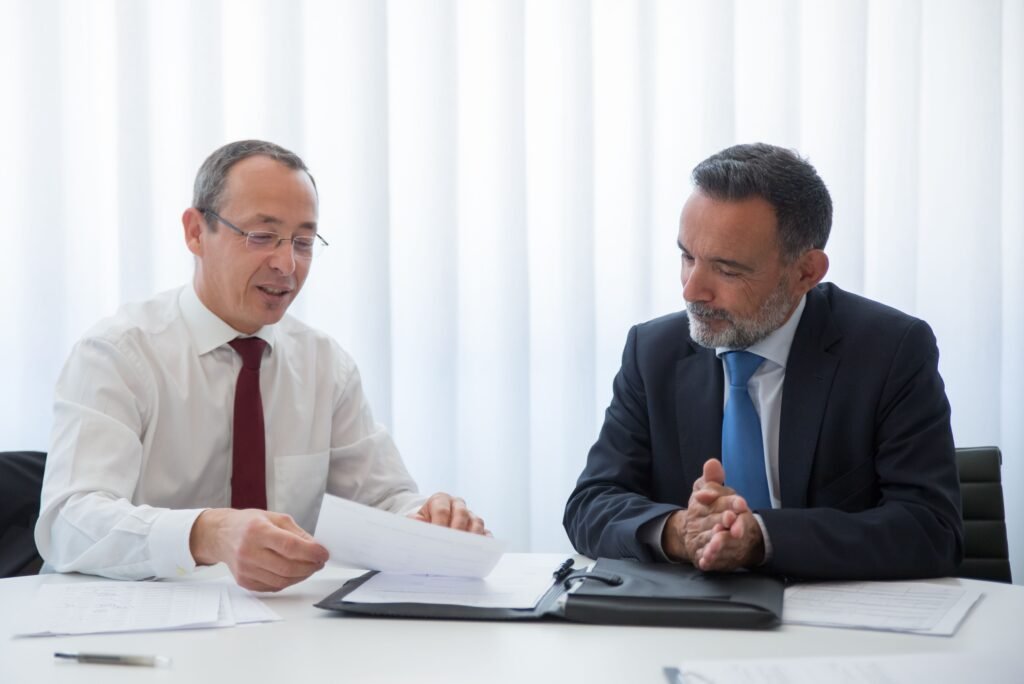 Two people side by side at a desk, one reading from a stapled document in a folder.